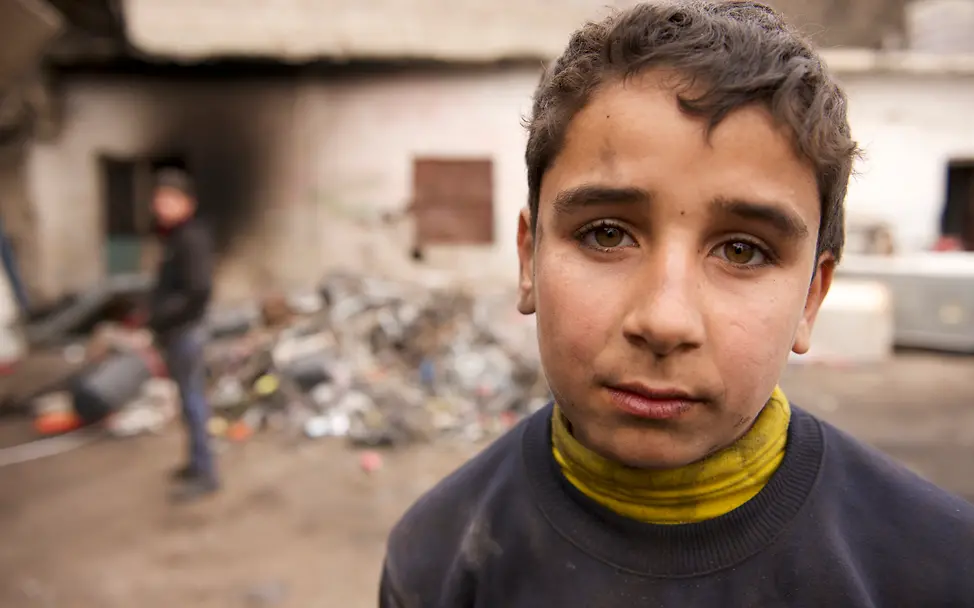 Der 14-jährige Ahmed steht vor der Recycling-Anlage. Sein Blick zeigt wie anstrengend die Arbeit für ihn ist.