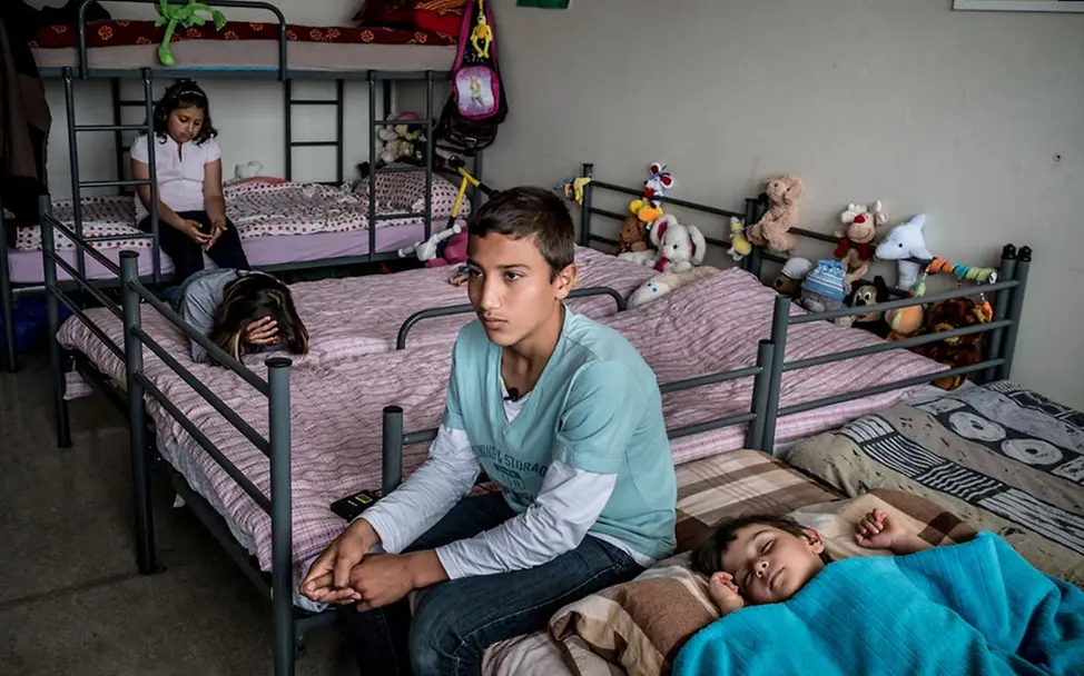 Chimen sitzt im Zimmer seiner Flüchtlingsunterkunft | © UNICEF/Ashley Gilbertson UNICEF-Bericht: Chimen teilt sich mit drei Geschwistern ein Zimmer in der Flüchtlingsunterkunft