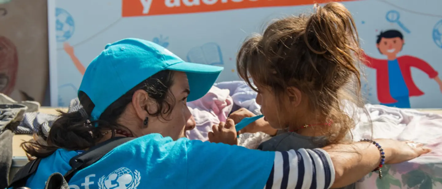 UNICEF-Helferin spricht mit einem Mädchen, das gerade seine Zähne putzt. 