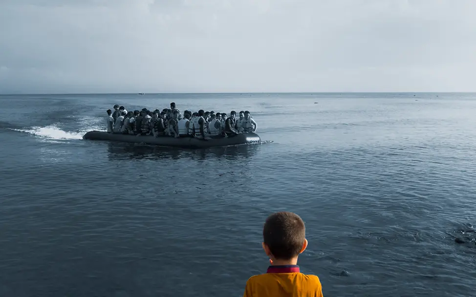 Ein Junge blickt auf das Meer in Lesbos, Griechenland hinaus, wo gerade ein Boot mit Flüchtlingen ankommt.