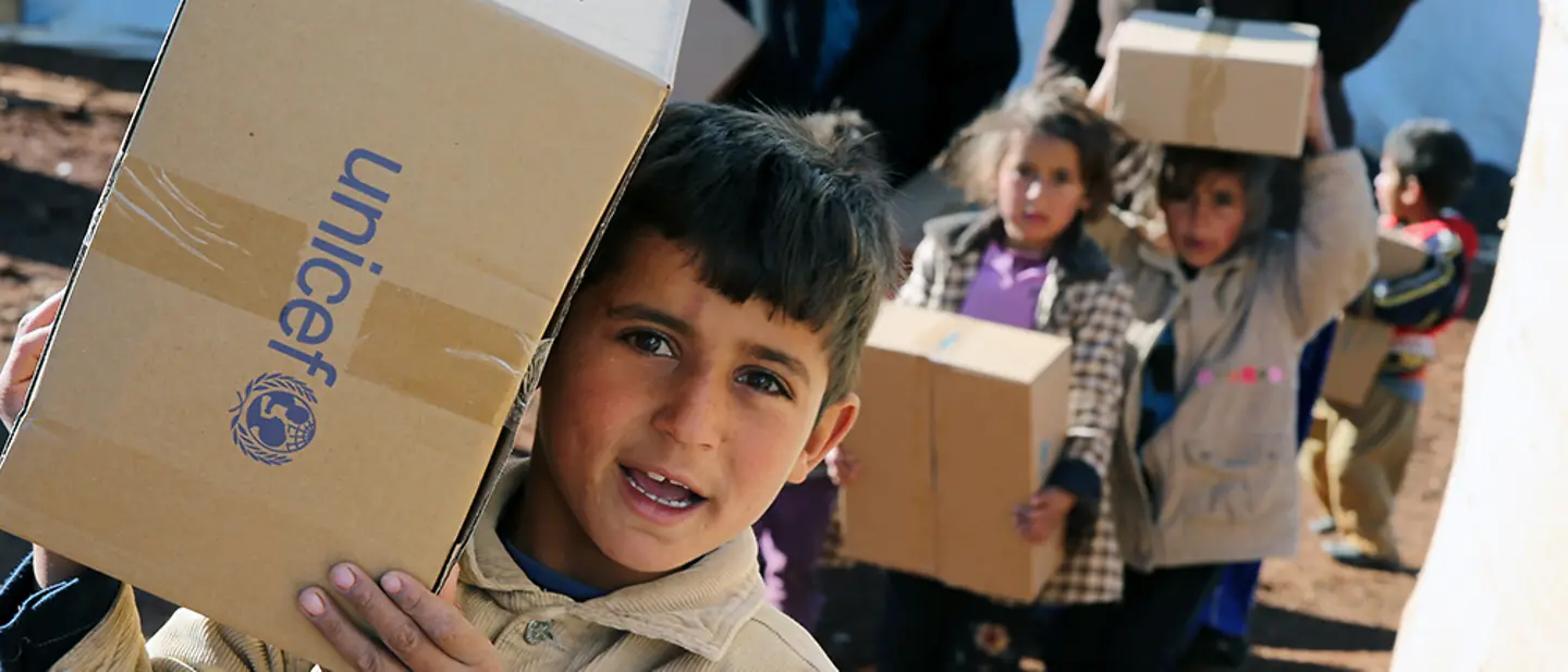 Der Weg der Spende: Ein Junge trägt eine UNICEF-Kiste. Hinter ihm sind weitere Kinder mit Hilf-Kartons.