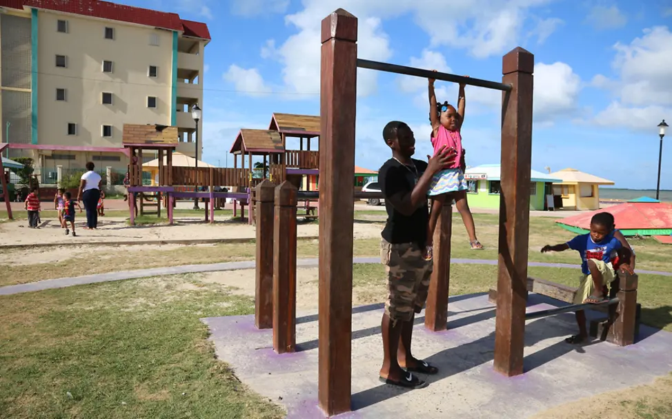 Andrew hilft seiner kleinen Schwester beim Turnen | © UNICEF/LeMoyne Belize: Kinder spielen auf einem Spielplatz in Belize City