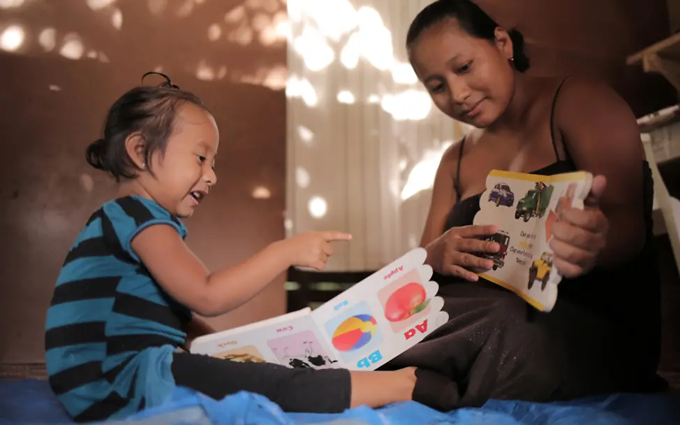 Glenda lernt mit ihrer Tochter das Alphabet | © UNICEF/LeMoyne Belize: Tyra sitzt auf einem Bett und lernt das Alphabet