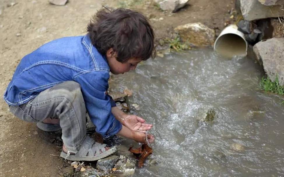Verunreinigtes Wasser ist lebensgefährlich für Kinder. | © UNICEF/Alsamai Kind schöpft mit den Händen Wasser neben einem Abwasserrohr und riskiert damit eine Choleraerkrankung.