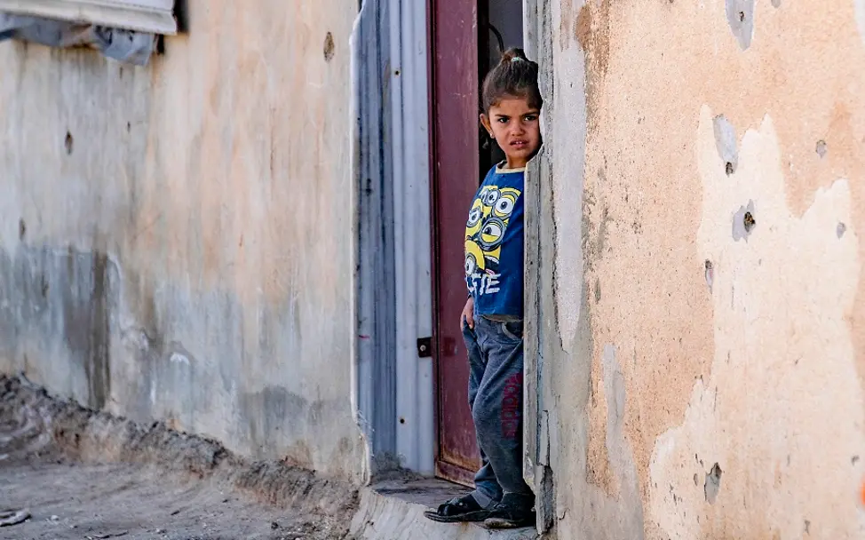 Neben Einschusslöchern in der Wand: Ein Mädchen im Nordosten von Syrien. | © UNICEF/Keder Syrien: Ein Mädchen steht in einer Haustür. Die Wand des Hauses ist gezeichnet von Einschusslöchern.
