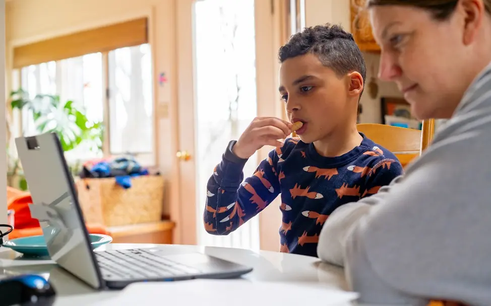 Online in der Schule während der Covid-19-Pandemie. | © UNICEF/McIlwaine Ein achtjähriger Junge sitzt mit seiner Mutter zuhause vor einem Laptop.