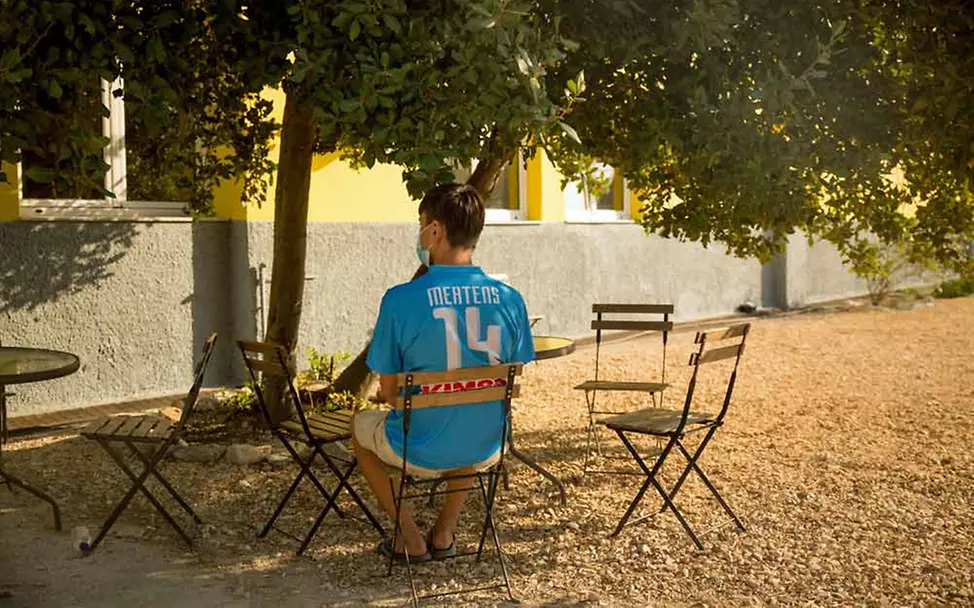 Endlich in Sicherheit: Bahnam aus Afghanistan sitzt im Hof der Notunterkunft. | © UNICEF/Christophilopoulos Bahnam sitzt im Hof der Notunterkunft Tapuat auf einem Stuhl unter einem Baum.