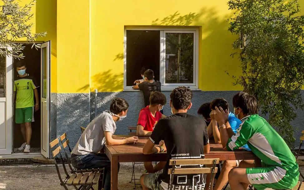 Nach dem Großbrand in Moria können die Jugendlichen in der Notunterkunft entspannen. | © UNICEF/Christophilopoulos Mehrere geflüchtete Jugendliche sitzen zusammen im Hof des Kinderzentrums an einem Tisch.