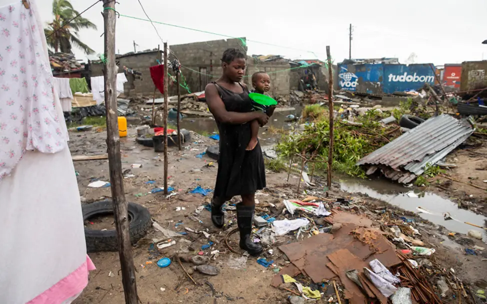 Zyklon Idai: Eine Frau mit Baby auf dem Arm geht durch eine zerstörte Siedlung | © UNICEF/de Wet AFP-Services Zyklon Idai: Eine Frau mit einem Baby auf dem Arm geht durch Trümmer