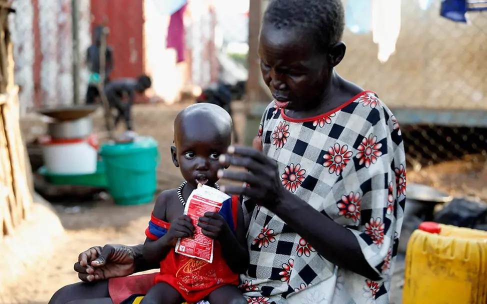 Hungersnot Afrika verhindern: Ein mangelernährtes Kleinkind hält auf dem Schoß seiner Oma ein Päckchen Erdnusspaste in der Hand.
