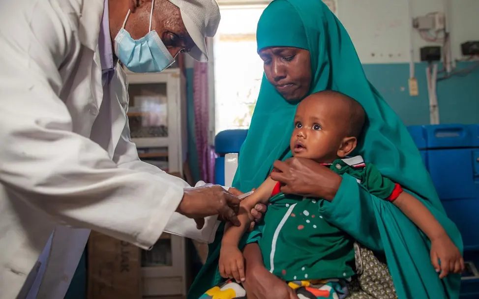 Impfung gegen Masern | © UNICEF/Naftalin Ein Kind in Somalia wird auf dem Schoß seiner Mutter gegen Masern geimpft.