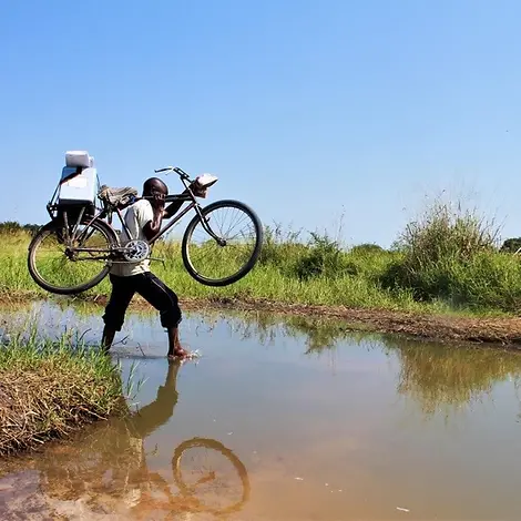 Demokratische Republik Kongo: Ein Helfer trägt Hilfsgüter auf einem Fahrrad über einen Fluss.