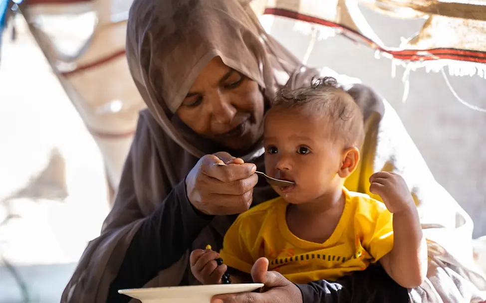 I UNICEF/Mojtba Moawia Mahmoud Eine Mutter füttert ihren Sohn, der auf ihrem Schoß sitzt.