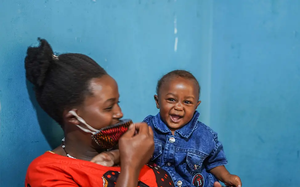 Uganda: Eine Mutter wartet auf ihre Corona-Schutzimpfung | © UNICEF/Abdul Corona: Eine Mutter in Uganda spielt mit ihrem Baby, während sie auf eine Corona-Schutzimpfung wartet.