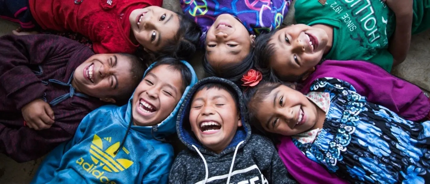 Sieben Kinder liegen zusammen in einem Kreis und lachen.