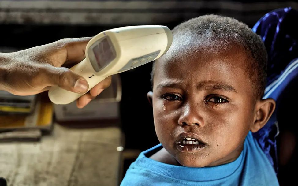Malaria: Einem weinenden dreijährigen Jungen wird ein Fiebermesser an die Stirn gehalten. 