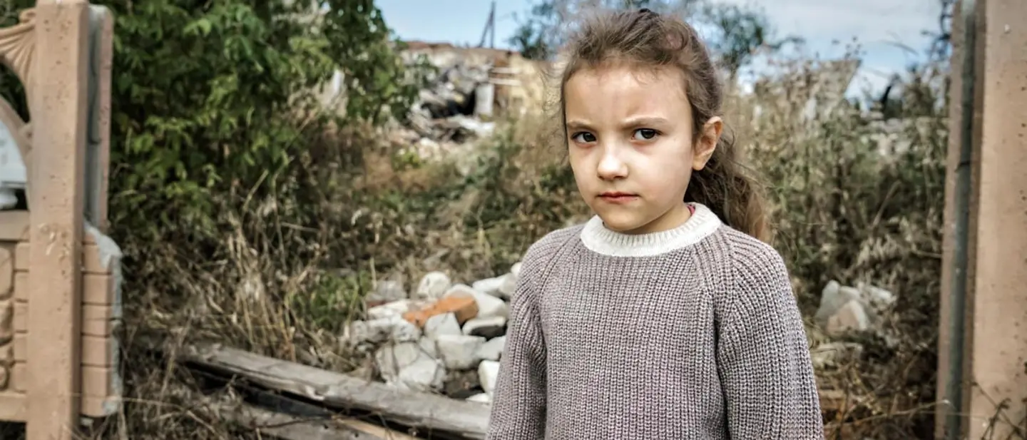 Ukraine Spenden: Ein Mädchen in der Charkiw-Region steht vor einer im Krieg zerstörten Schule.