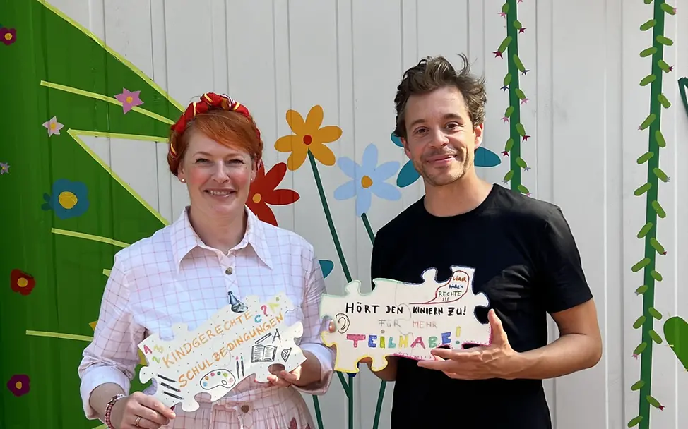 Weltkindertag: Tobias Krell und Enie van de Meiklokjes halten kreativ gestaltete Kinderrechte-Puzzleteile in den Händen 