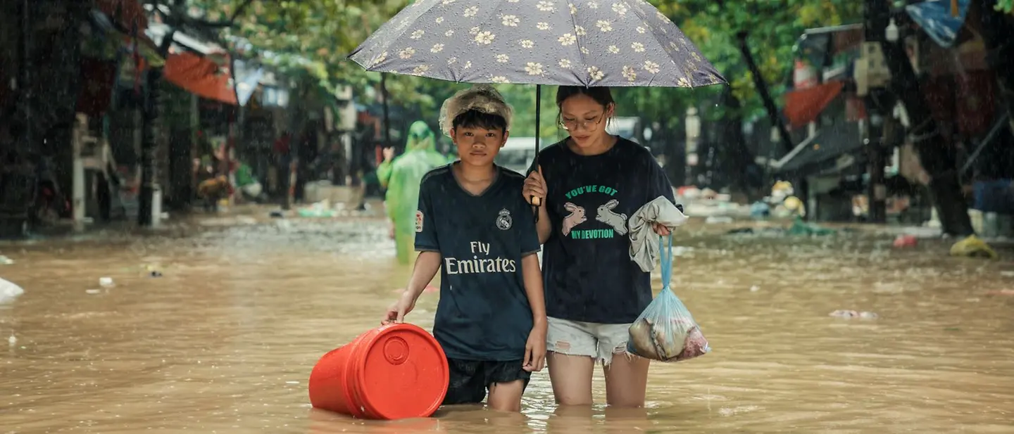 Zwei Mädchen laufe durch knietiefes Wasser in Thai Nguyen, Vietnam,  nach dem Taifun Yagi.