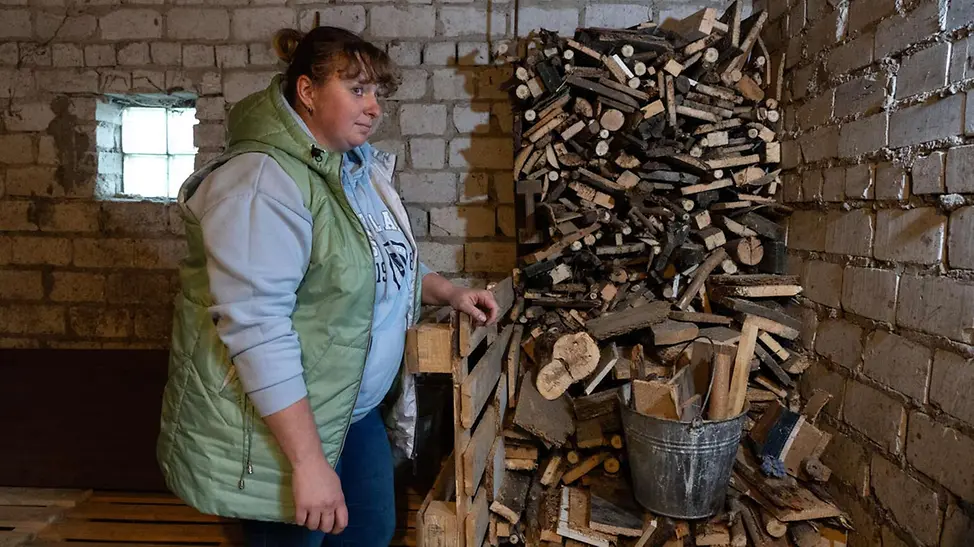 Ukraine Winter Hilfe: Eine geflüchtete Mutter in der Ukraine steht vor einem Stapel Brennholz für den Winter 