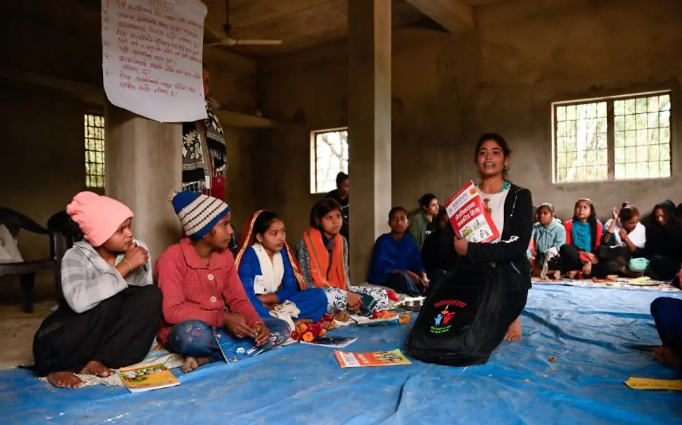 Mädchen sitzen in einem Gemeindzentrum und  erfahren, wie sich zur Schule anmelden können.