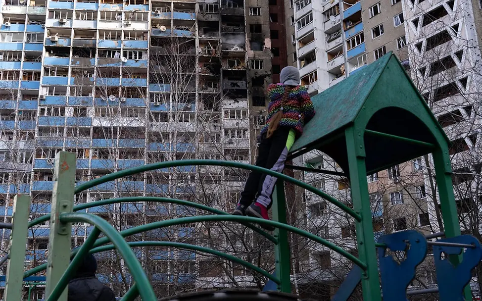 Ein Mädchen auf einem Spielplatz in Kiew vor zerstörten Wohnungen. | © UNICEF/Filippov Ein Mädchen auf einem Spielplatz in Kiew vor zerstörten Wohnungen