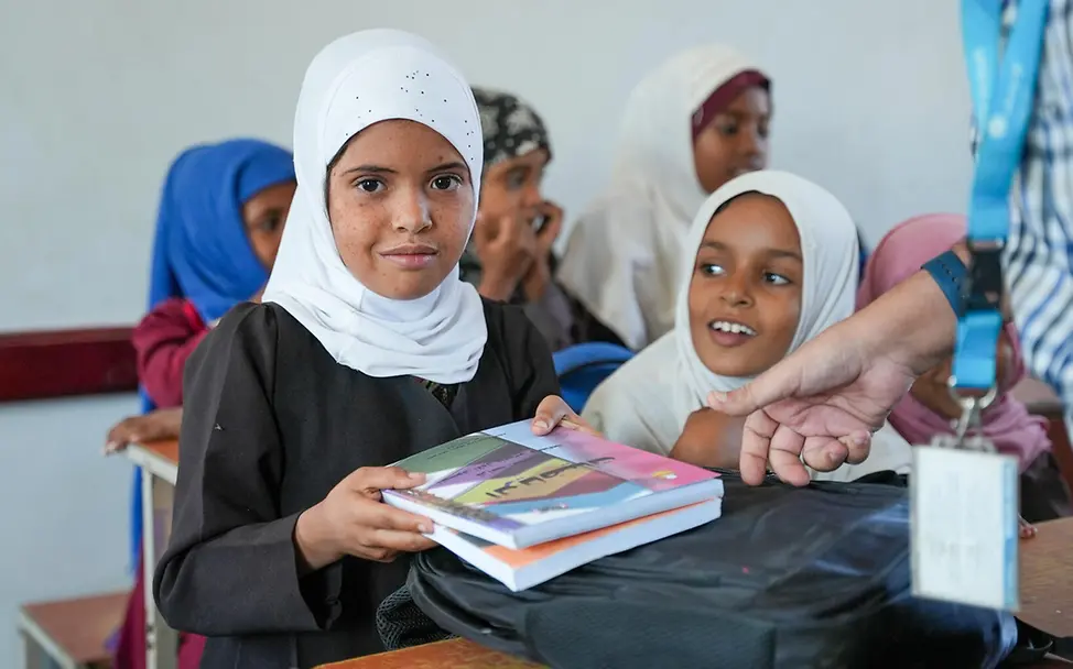 Spenden für den guten Zweck: Ihre Spende trägt dazu bei, Kindern weltweit Bildung und bessere Chancen zu ermöglichen. | UNICEF/Al-Maqtari Originelle Geschenkideen für den guten Zweck: Zwei Mädchen an einem Schultisch zeigen ihre neuen Bücher.