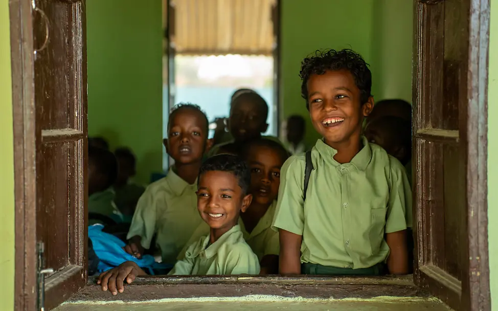 Schenken für den guten Zweck: Spenden an UNICEF ermöglichen Kindern weltweit mehr Zugang zu Bildung. | © UNICEF/Rajab Originelle Geschenkideen für einen guten Zweck: Zwei Jungen schauen lächelnd aus dem Fenster ihrer Schule im Sudan.