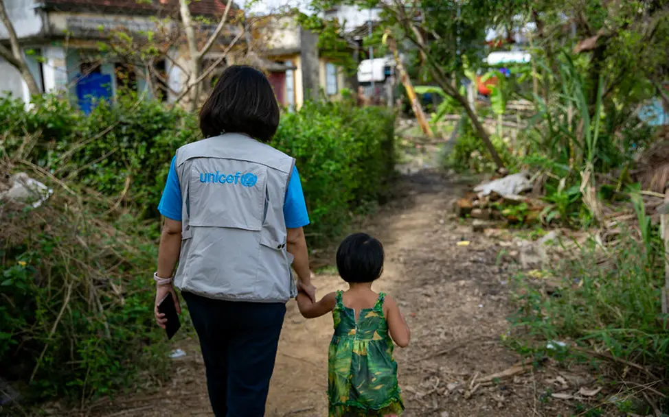 Schenken für den guten Zweck: Ihre Spende hilft UNICEF, Kinder dort zu unterstützen, wo am dringendsten Hilfe nötig ist. | © UNICEF/Luu Thu Huong Originelle Geschenkideen für einen guten Zweck: Eine UNICEF-Helferin geht mit einem kleinen Mädchen an der Hand.