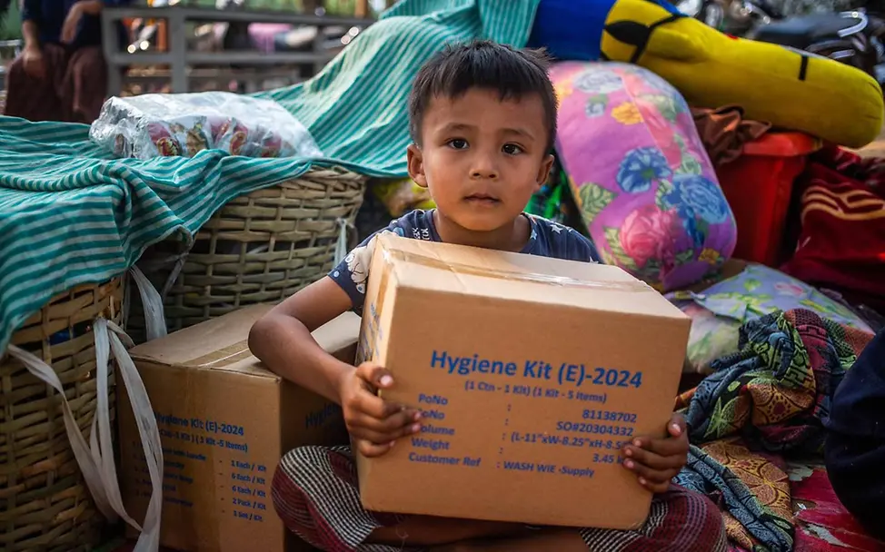 Schenken für den guten Zweck: Ihre Spende hilft, Kinder auf der ganzen Welt mit lebensrettenden Hilfsgütern zu versorgen. | © UNICEF/Htet Originelle Geschenkideen für einen guten Zweck: Ein kleiner Junge hält einen Karton mit Hilfsgütern.
