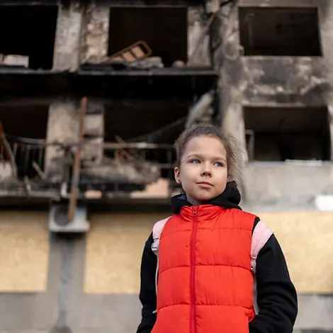 Myroslava (8) steht vor einem zerbombten Wohnhaus, das einmal ihr Zuhause war.