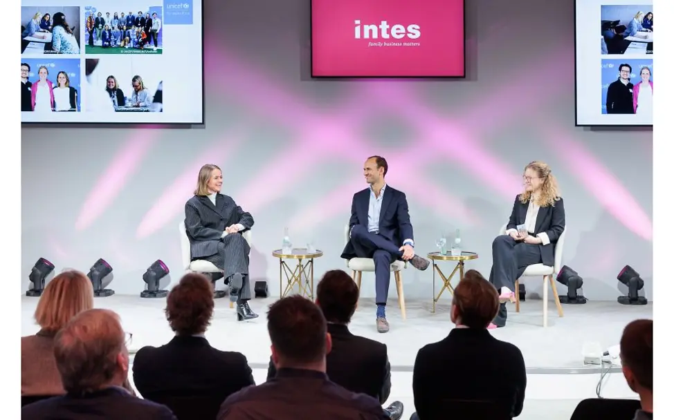 Panel sitzt auf einer Bühne.