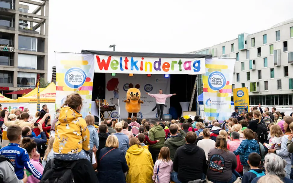 Weltkindertag einfach erklärt: Die Maus vor vielen Kindern auf einer Bühne