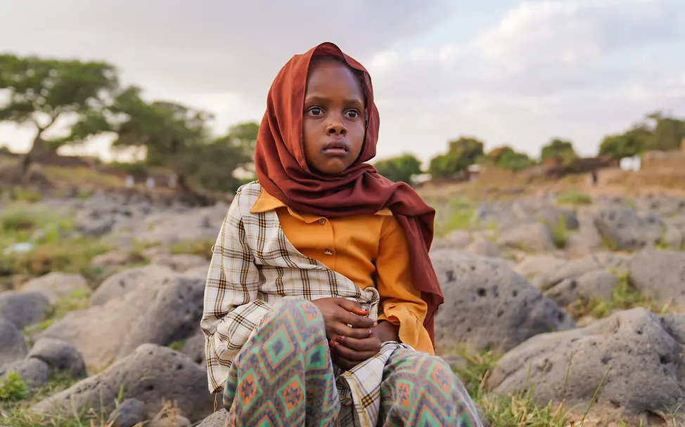 Die neunjährige Tuqaa floh aus Al-Fashir. | © UNICEF/UNI941674/Jamal Mädchen sitzt auf Steinen
