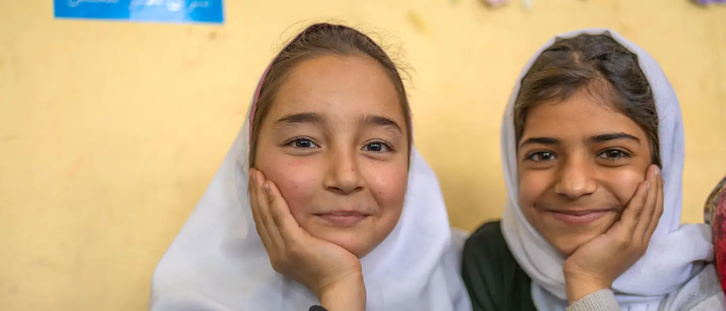 Zwei Mädchen in Afghanistan in einer Schule in Herat | © UNICEF/Khayyam Spenden für Mädchen: Zwei Mädchen in Afghanistan sitzen lächelnd in einem Klassenzimmer.