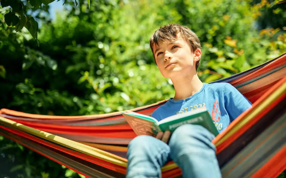 Grundgesetz einfach erklärt: Jeder Mensch in Deutschland darf an das glauben, was er oder sie möchte | © UNICEF/Bänsch Grundgesetz einfach erklärt: Ein Junge mit einem Buch sitzt in einer Hängematte.