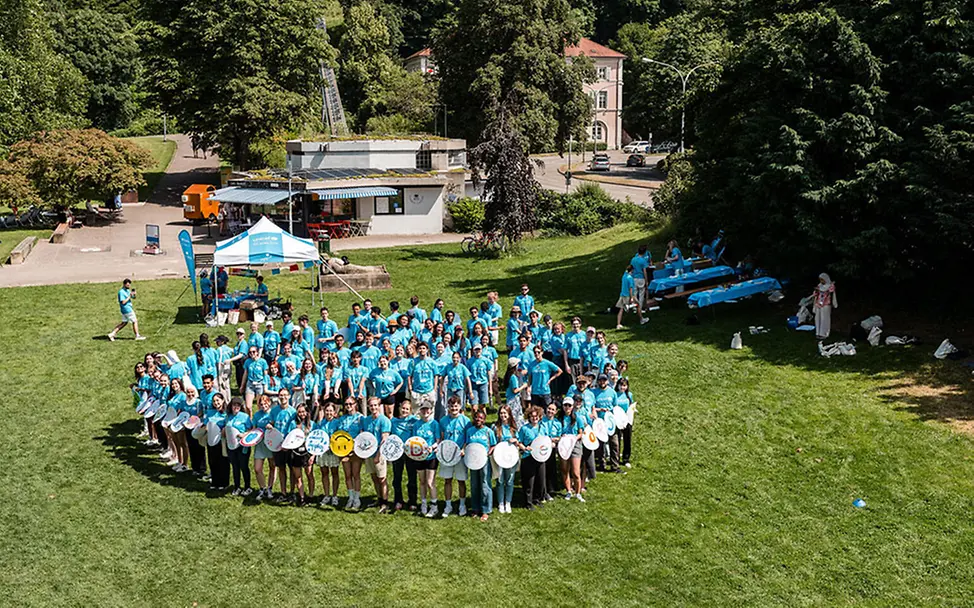 UNICEF-Hochschulgruppe aus Freiburg beim jährlichen Treffen. | © UNICEF/Conklin Freiwilligenarbeit junge Erwachsene: Viele junge Erwachsene mit UNICEF-Shirts stehen im Kreis auf einer Wiese.