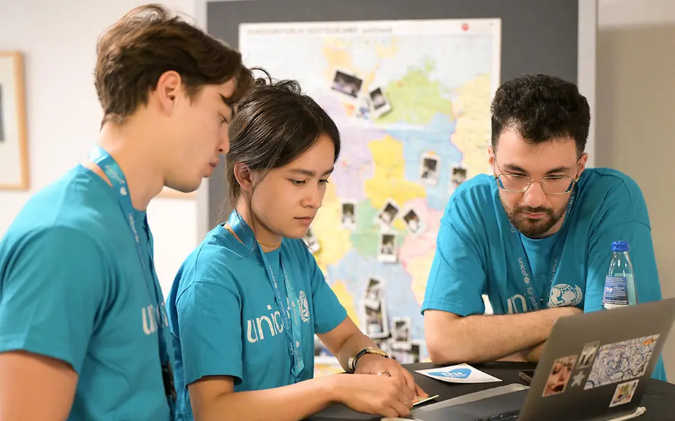 UNICEF-Hochschulgruppe aus Freiburg beim jährlichen Treffen. | © UNICEF/Sachse-Grimm 3 UNICEF-Engagierte stehen an einem Tisch und schauen gemeinsam auf einen Laptop.