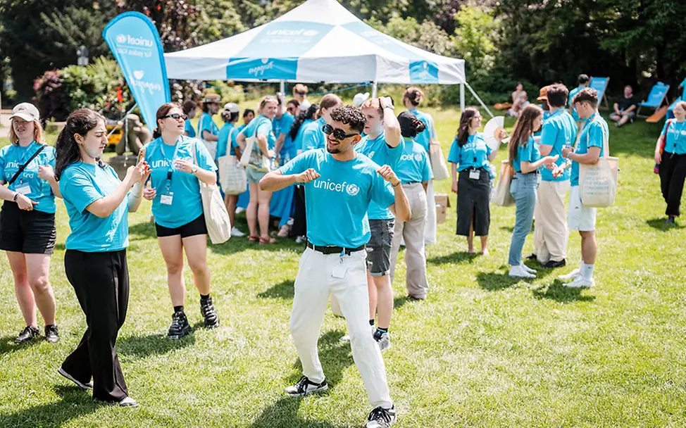 UNICEF-Hochschulgruppe aus Freiburg beim jährlichen Treffen. | © UNICEF/Conklin Freiwilligenarbeit junge Erwachsene: Viele junge Erwachsene mit UNICEF-Shirts tanzen und reden auf einer Wiese.