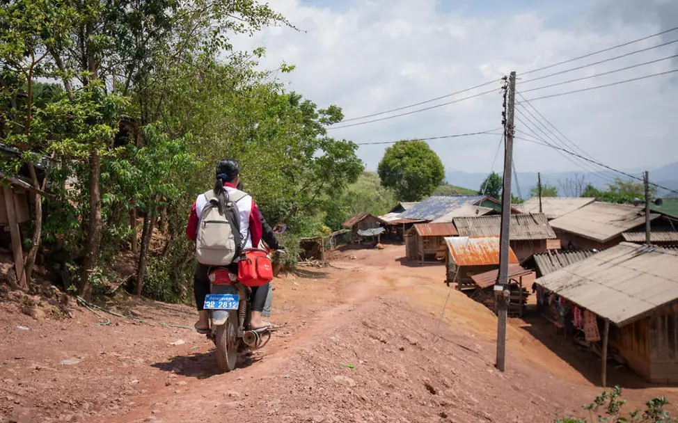 Die Helfer*innen von UNICEF nehmen jeden Weg auf sich, um Impfstoffe zu den Kindern zu bringen. | © UNICEF/Phiennachit Impfen einfach erklärt: Zwei Gesundheitshelfer*innen fahren mit dem Motorrad auf einem schmalen Weg.