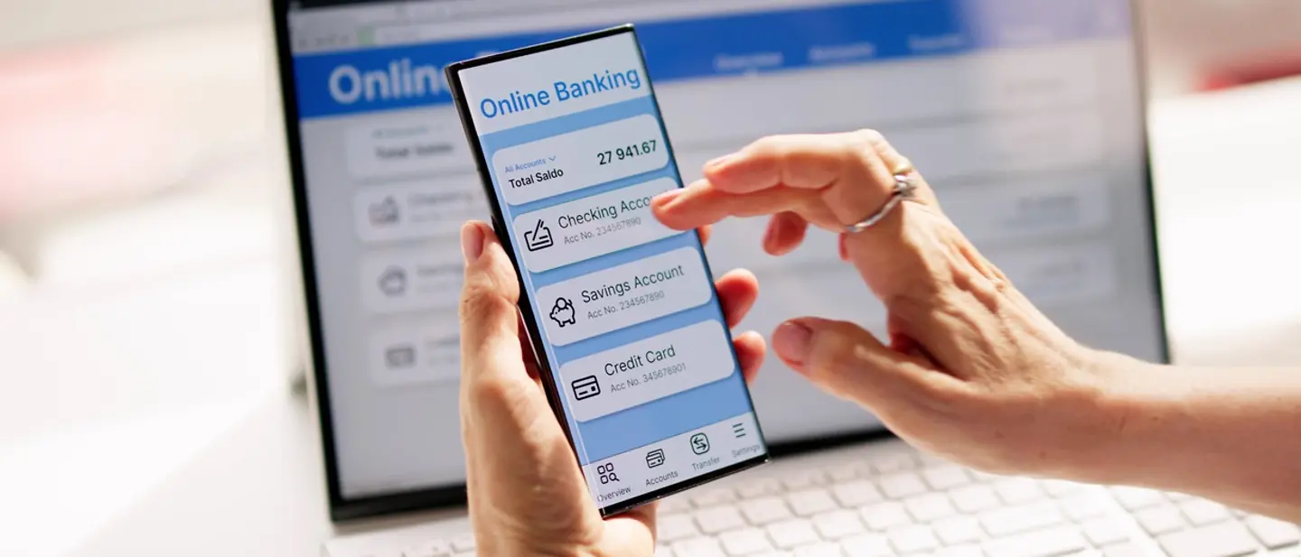Digitale Vorsorge ist entscheidend, damit Hinterbliebene Zugriff auf das digitale Erbe haben. Digitaler Nachlass: Zwei Hände halten ein Smartphone mit einer Onlinebanking-App auf dem Bildschirm.