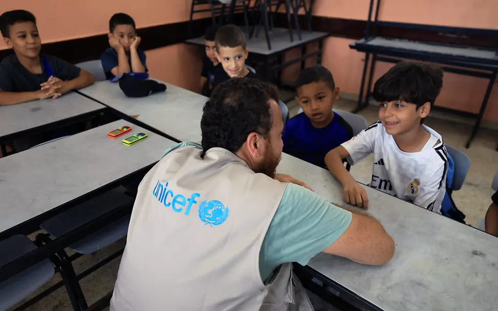 Ein UNICEF-Helfer unterhält sich in einem Klassenzimmer mit Kindern | © UNICEF/Izhiman Westjordanland Aufwachsen spenden: Ein UNICEF-Helfer unterhält sich in einem Klassenzimmer mit palästinenischen Jungen.