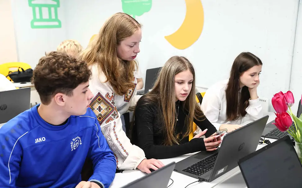 Bildung einfach erklärt: Eine Lehrerin und Schüler arbeiten an Laptops.