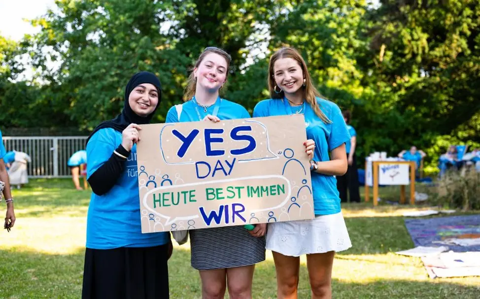 Schulaktion zum Tag der Kinderrechte: Drei Mädchen halten ein großes Schild mit der Aufschrift Yes Day.