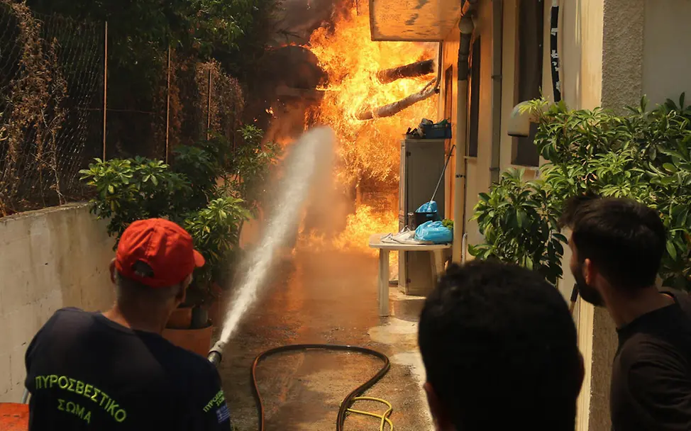 Waldbrand Folgen: Zwei Feuerwehrleute löschen ein Feuer in der Nähe eines Wohnhauses.